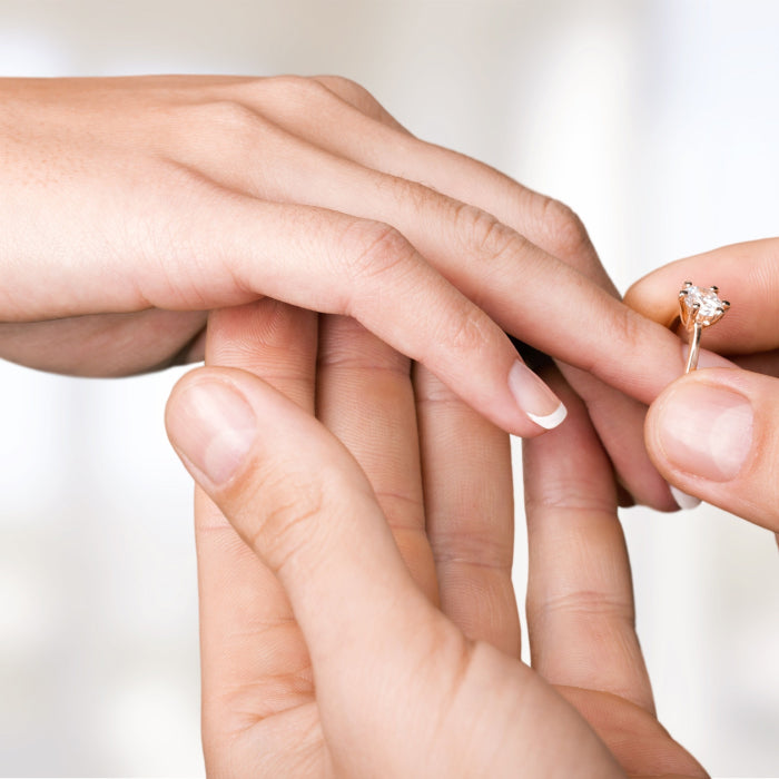 Man placing diamond engagement ring on a lady's finger